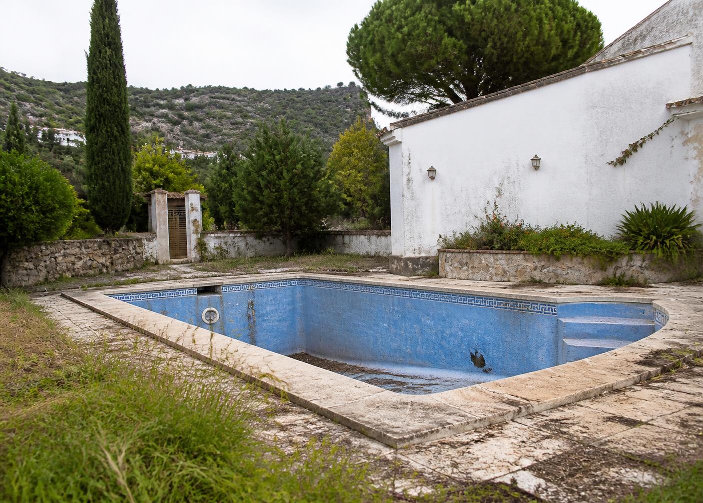 Piscina antigua vacía, con el revestimiento agrietado y el entorno descuidado